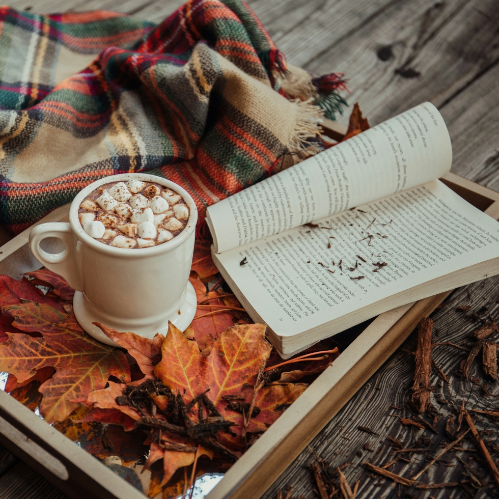 Aufgeschlagenes Buch mit heißer Schokolade, Decke und Herbstblättern