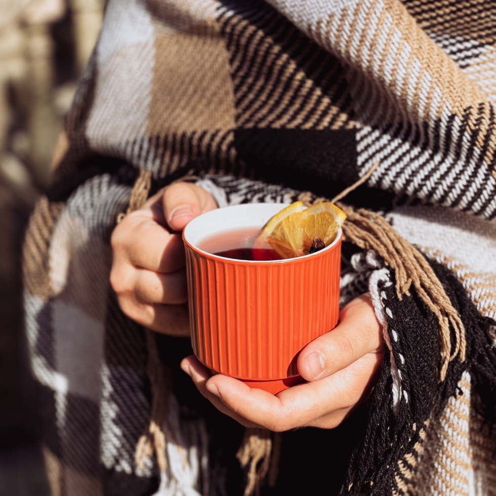 Punsch Rezeptideen: Eine Tasse mit Orangenpunsch wird mit beiden Händen gehalten, die Person ist in eine karierte Wolldecke gehüllt.