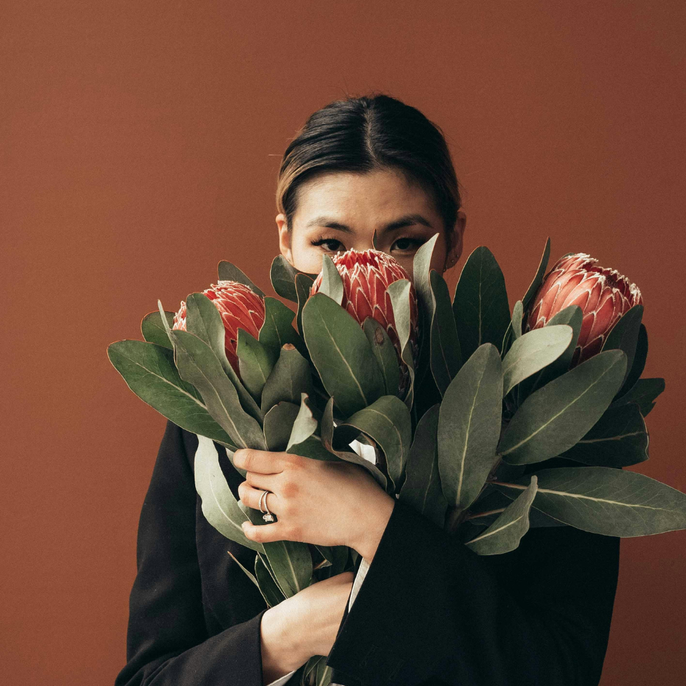 Geschenkideen Sternzeichen Schütze: Eine Frau hält einen großen Blumenstrauß vor ihrem Gesicht.