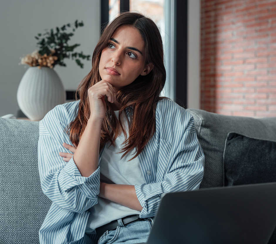 Frau mit laptop sitzt am Sofa und grübelt.