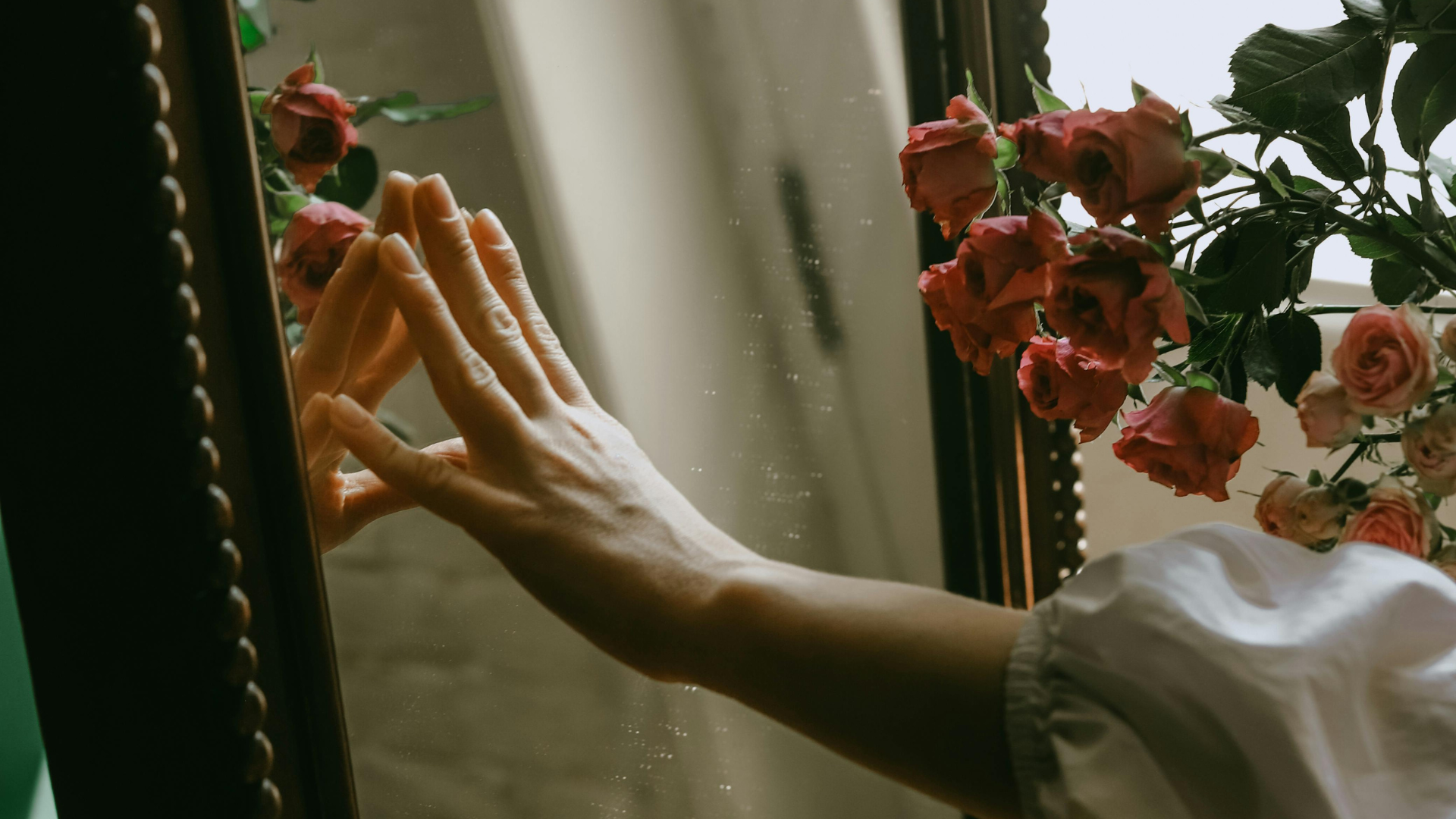weibliche Hand auf spiegel mit rosen im hintergrund, aesthetic