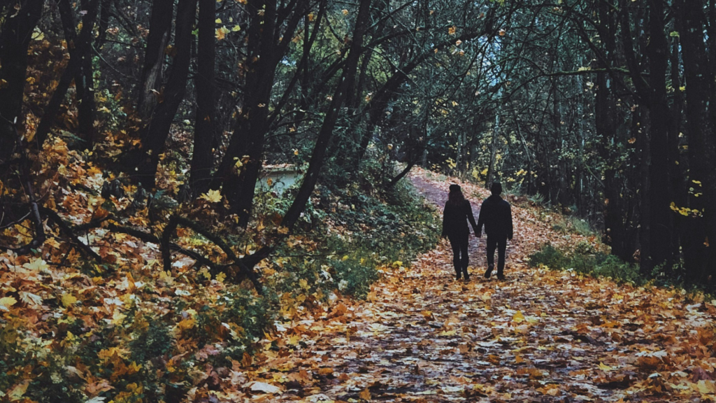 Lebeshoroskop für den Herbst 2025: Ein Paar geht Hand in Hand durch einen Wald, Herbstlaub liegt auf dem Boden