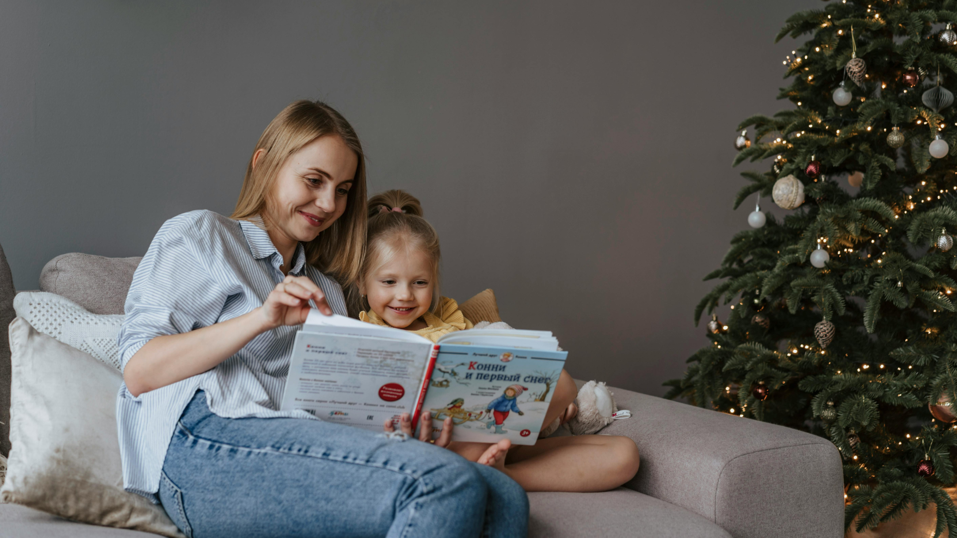 Frau lest Kind Buch vor auf dem Sofa beim Christbaum