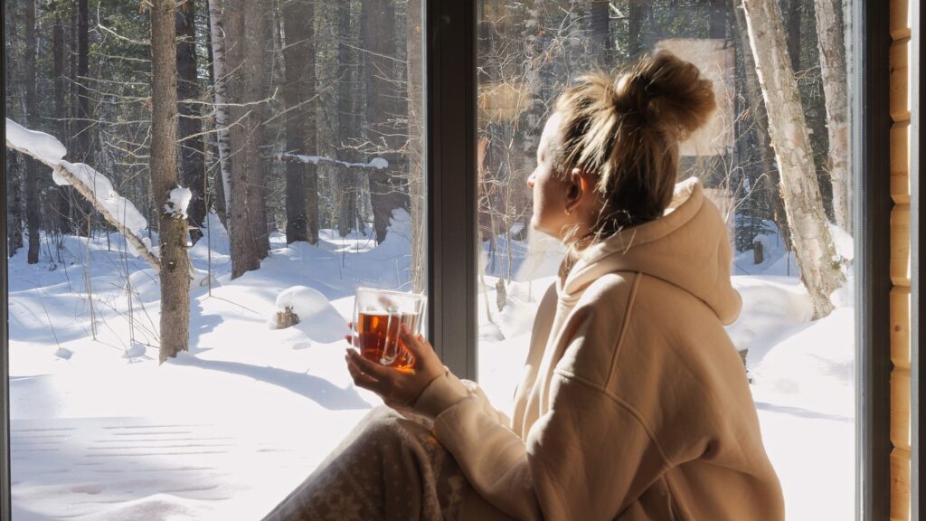 Frau sitzt vor Fenster und schaut in die schneebedeckte Natur
