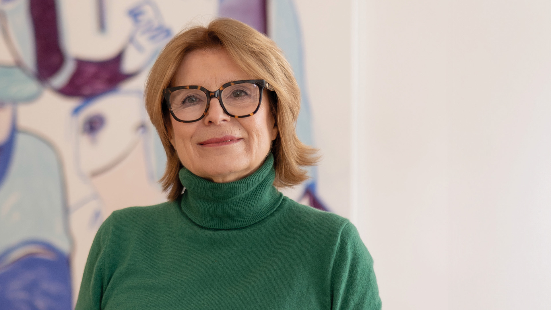 Edit Schlaffer: Frau mit Brille und grünem Rollkragenpullover blickt lächelnd in die Kamera