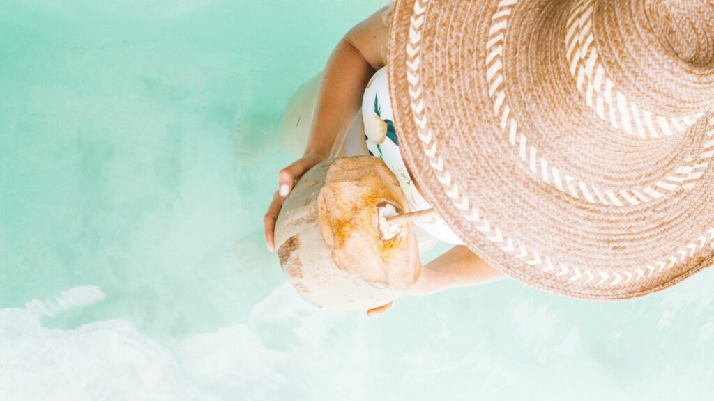 Frau im Wasser mit Kokosnuss in der Hand und Strohhut am Kopf